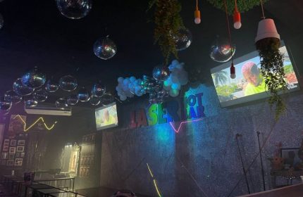 Interior of Laser Hot Bar, a gay bar in Cancun, Mexico. Disco balls hang from the ceiling. TVs play videos. Neon sign.