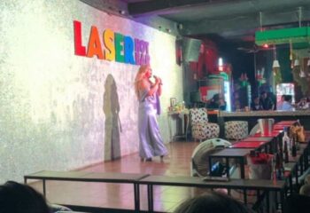 Drag queen performing at Laser Hot Bar, a popular gay bar in Cancun. Nightlife scene with stage, bar, and audience.