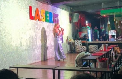 Drag queen performing at Laser Hot Bar, a popular gay bar in Cancun. Nightlife scene with stage, bar, and audience.
