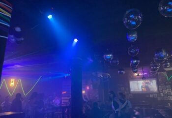 Inside Laser Hot Bar, a queer Cancun hotspot. Blue lights illuminate disco balls & patrons. A fun gay travel destination for men.
