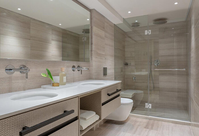 Dan Tel Aviv Hotel bathroom. Modern design with double sinks, light stone walls, and glass shower. Gay honeymoon travel inspiration.