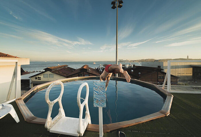 Sunset Destination Hostel: Man diving into rooftop pool. Best gay hostel in Lisbon with terrace. Lisbon skyline view.