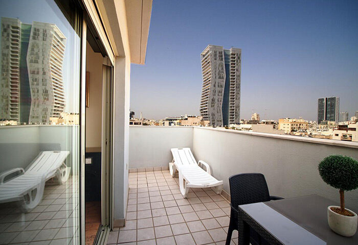 Ben Yehuda Apartments penthouse balcony view in Tel Aviv's gayborhood. Service apartment with skyline, table, chair, and lounge chair.