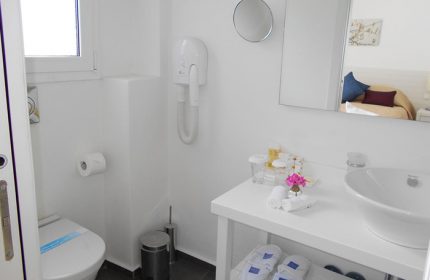 Bathroom at Portobello Boutique Hotel, Mykonos. Budget gay hotel in Mykonos Town gayborhood. White interior with toilet, sink, & amenities.
