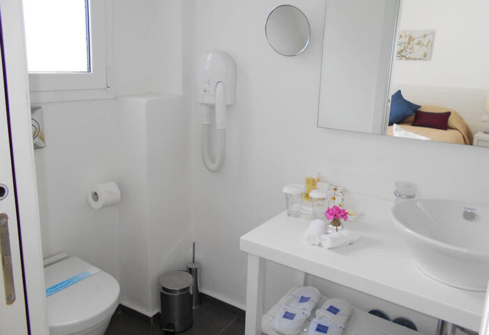 Bathroom at Portobello Boutique Hotel, Mykonos. Budget gay hotel in Mykonos Town gayborhood. White interior with toilet, sink, & amenities.