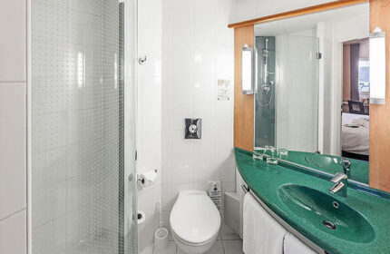 Ibis Praha Old Town hotel bathroom. Shower, toilet, and green sink. Gay hotels Prague city center. Modern, clean design.