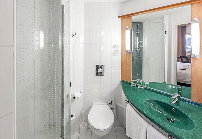 Ibis Praha Old Town hotel bathroom. Shower, toilet, and green sink. Gay hotels Prague city center. Modern, clean design.
