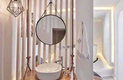 Stylish decor at Absolute Mykonos Suites, a gay hotel in Mykonos. Cool bathroom design with a round mirror, rope accents, & modern sink.
