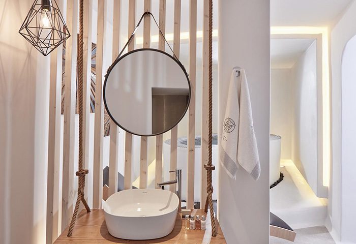 Stylish decor at Absolute Mykonos Suites, a gay hotel in Mykonos. Cool bathroom design with a round mirror, rope accents, & modern sink.
