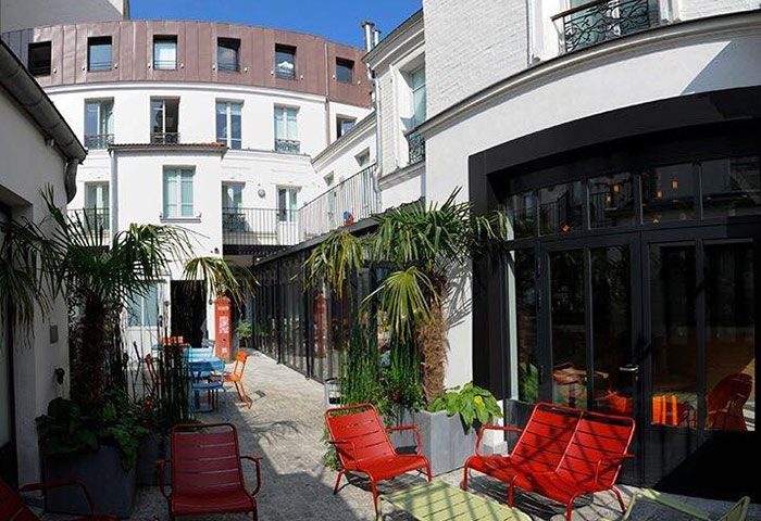 The 3 Ducks Eiffel Tower by Hiphophostels: Outdoor courtyard with colorful seating, plants, and white buildings. Gay hostel near nightlife.