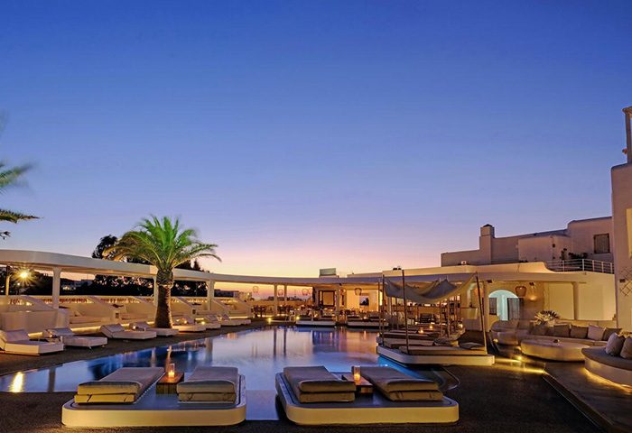 Andronikos Hotel upscale outdoor swimming pool at dusk. Gay travel destination with luxury sunbeds and palm trees. Mykonos hotel.