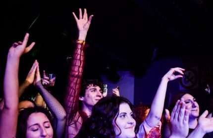Enthusiastic crowd at Latte Fresco, Rome's gay bar. People with hands raised, enjoying the vibrant nightlife. Gay travel advice.