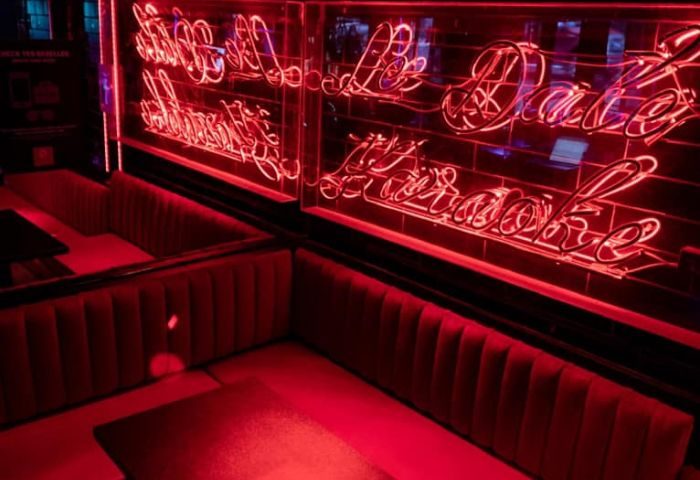 Interior of Le Date Gay Karaoke Bar in Montreal. Red neon sign and plush seating create a vibrant, inviting atmosphere.