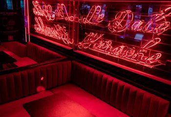 Interior of Le Date Gay Karaoke Bar in Montreal. Red neon sign and plush seating create a vibrant, inviting atmosphere.