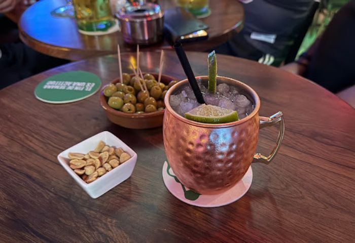 Le Mixx Gay Bar in Gran Canaria: Cocktail in a copper mug with peanuts and olives on a wooden table. Gay travel advice.