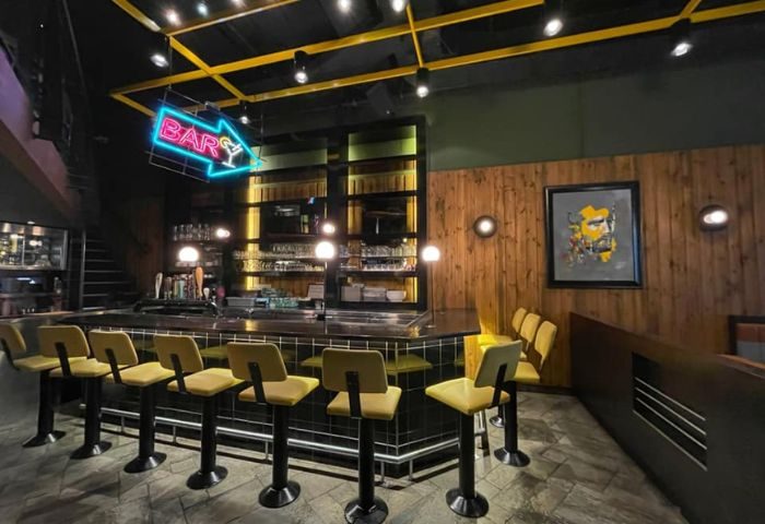 Interior of Le Saloon Gay Bar in Montreal. Bar stools line the bar under a neon BAR sign. Gay travel advice.