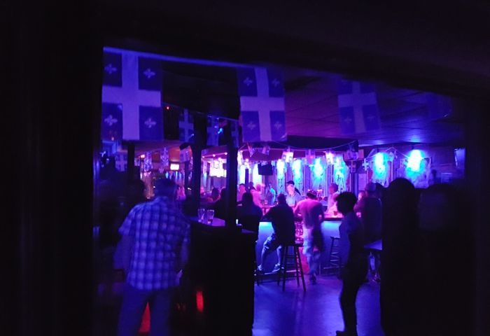 Le Stud Gay Bar in Montreal. Interior view of the bar with patrons, Quebec flags, and blue lighting. Gay travel advice.