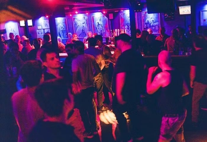 Montreal gay bar scene: Le Stud bar interior, crowded with gay men. Red and blue lighting, artwork on the walls. Gay travel advice.