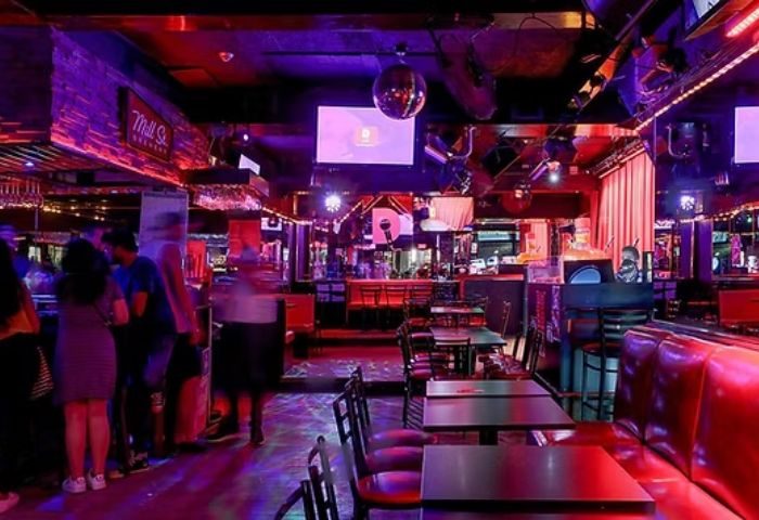Interior of Le Stud gay bar in Montreal. Red lighting, tables, chairs, disco ball, bar area, and patrons create a lively atmosphere.