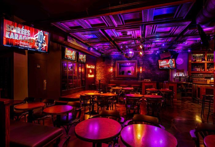 Interior of Le Taverne Normandie, a gay bar in Montreal. Tables and chairs fill the room, lit with purple and blue lights. Karaoke nights.