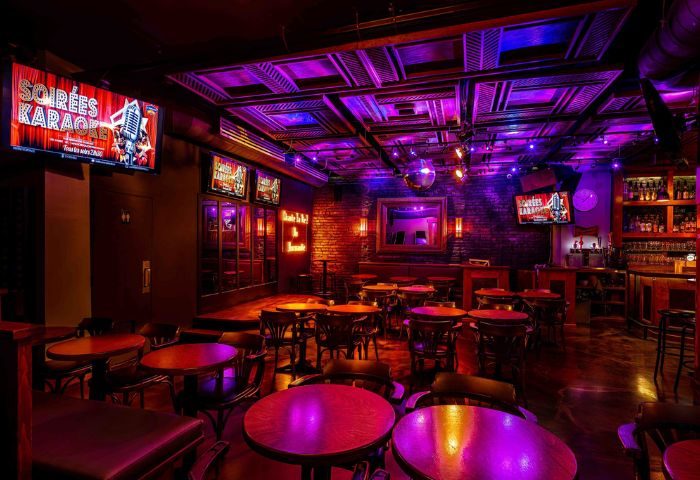 Interior of Le Taverne Normandie, a gay bar in Montreal. Tables and chairs fill the room, lit with purple and blue lights. Karaoke nights.