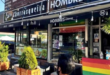 Hombre's Lounge, a gay bar in NYC. The lounge has a rainbow flag and a sign that says Cocktails & Food 10-60. Gay men travel advice.