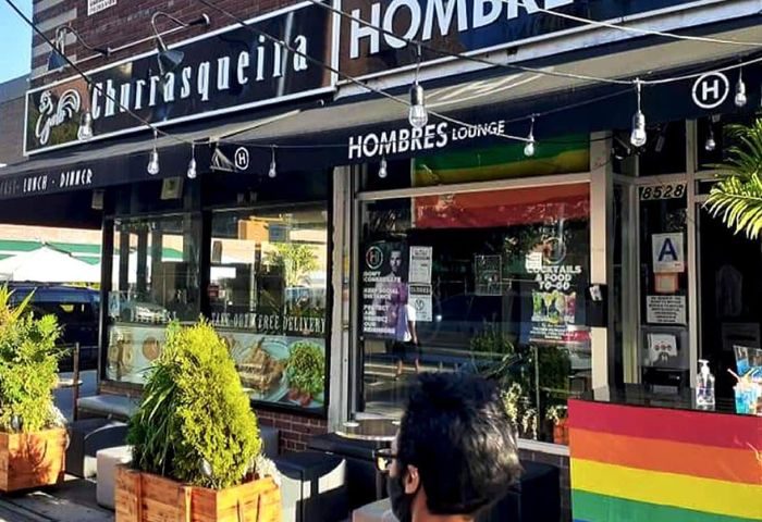 Hombre's Lounge, a gay bar in NYC. The lounge has a rainbow flag and a sign that says Cocktails & Food 10-60. Gay men travel advice.