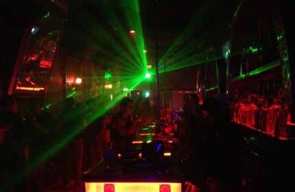 Les Hommes Gay Bar: Interior view of a crowded gay bar in New York with green laser lights and red bar lighting. Nightlife scene.