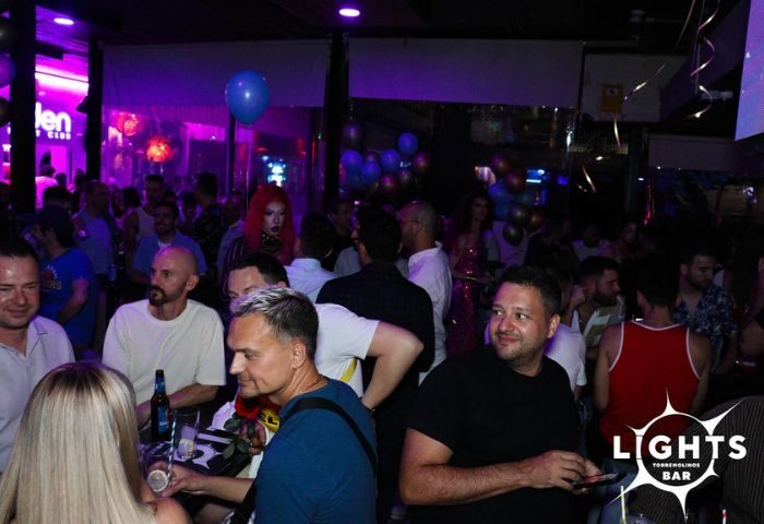 Lights Bar, a gay bar in Torremolinos. A crowded scene with men enjoying drinks and socializing in a vibrant, purple-lit atmosphere.