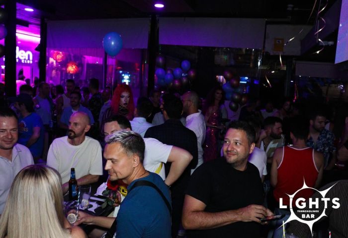 Lights Bar, a gay bar in Torremolinos. A crowded scene with men enjoying drinks and socializing in a vibrant, purple-lit atmosphere.