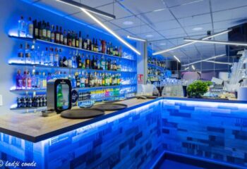 Interior of a gay bar in Torremolinos, Spain. Shelves of liquor bottles behind a bar with blue lights. Gay travel destination.