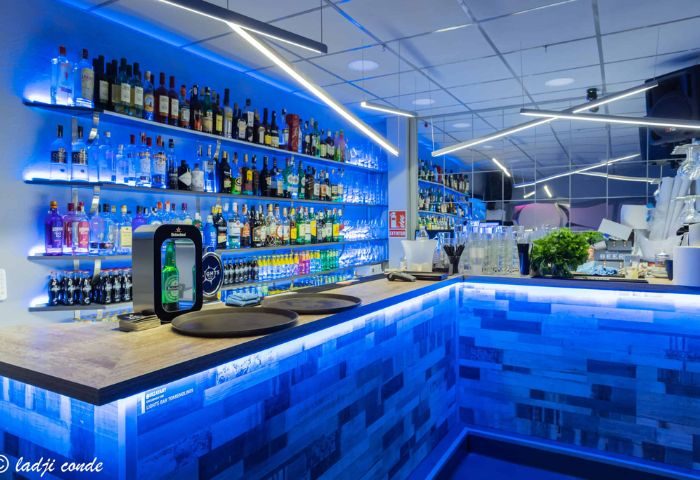 Interior of a gay bar in Torremolinos, Spain. Shelves of liquor bottles behind a bar with blue lights. Gay travel destination.