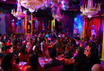 Lips Drag Queen Show Palace in New York. A crowded venue with a drag queen performing on stage, chandeliers, and disco balls.