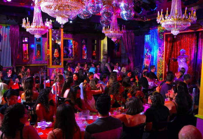 Lips Drag Queen Show Palace in New York. A crowded venue with a drag queen performing on stage, chandeliers, and disco balls.