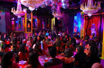 Lips Drag Queen Show Palace in New York. A crowded venue with a drag queen performing on stage, chandeliers, and disco balls.