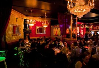 Lips Drag Queen Show Palace interior in New York. Patrons dine under chandeliers in the ornate, red-and-gold themed restaurant.