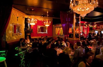 Lips Drag Queen Show Palace interior in New York. Patrons dine under chandeliers in the ornate, red-and-gold themed restaurant.