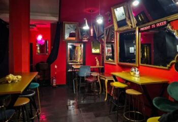 Interior of Lo de Carmen, a gay bar in Barcelona. Red walls, mirrors, tables, stools, and quirky decor create a unique, queer-friendly atmosphere.