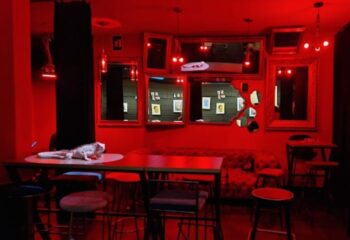Lo de Carmen Gay Bar in Barcelona: Red-lit interior with tables, stools, mirrors, and a decorative iguana. Gay travel advice.
