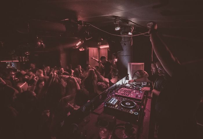 Lola's Club Ibiza gay club: DJ playing music to a dancing crowd. Nightlife scene with red lighting. Gay travel destination in Ibiza, Spain.