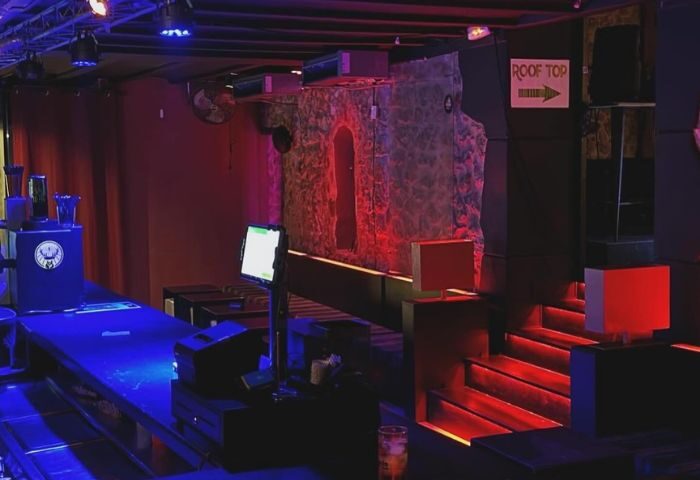 Lola's Club Ibiza gay club interior. Bar area with blue lighting, stone wall feature, and stairs to the rooftop. Ibiza gay nightlife.