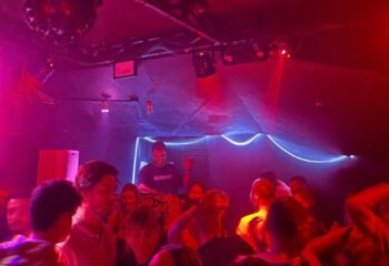 Lola's Club Ibiza gay club: DJ playing music to a crowd of people under red and blue lights. Nightlife scene in Ibiza for gay men.