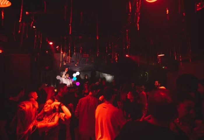 Inside Lola's Club Ibiza, a gay club. People dance under red lights, enjoying Ibiza's nightlife. A DJ plays music. Gay travel advice.