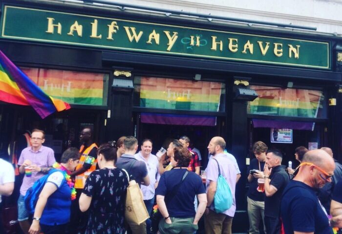 Halfway To Heaven, a gay bar in London's City Centre, features drag and karaoke. A crowd gathers outside, celebrating with rainbow flags.