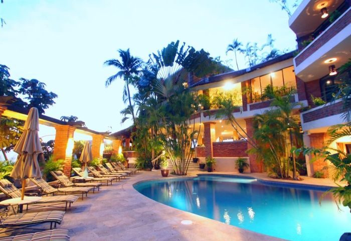 The Lookout gay bar in Puerto Vallarta. Poolside view with lounge chairs, tropical plants, and a building with balconies at dusk.