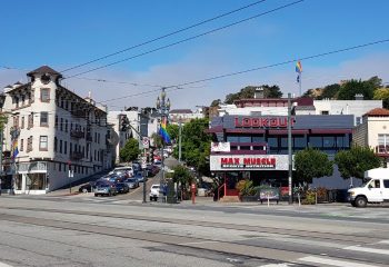 Street view of Lookout Gay Bar in San Francisco. Rainbow flags wave near the popular bar and Max Muscle. Cars line the steep hills.