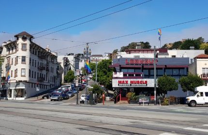 Street view of Lookout Gay Bar in San Francisco. Rainbow flags wave near the popular bar and Max Muscle. Cars line the steep hills.