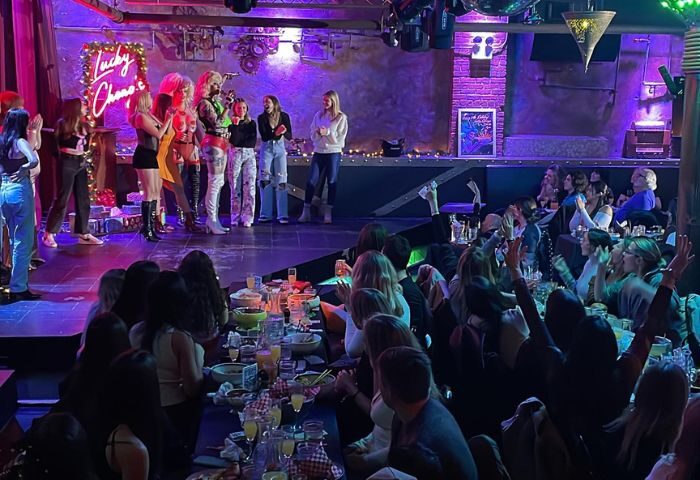 Lucky Cheng's Drag Cabaret in New York scene. Drag queens on stage being applauded by a crowd at tables. Gay travel destination.