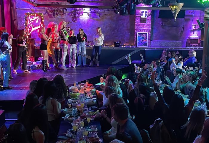 Lucky Cheng's Drag Cabaret in New York scene. Drag queens on stage being applauded by a crowd at tables. Gay travel destination.