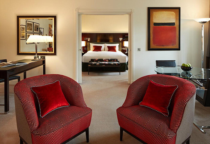 Sofitel St James London Hotel suite. Luxury gay hotel room for gay couples, featuring red armchairs and a view into the bedroom.